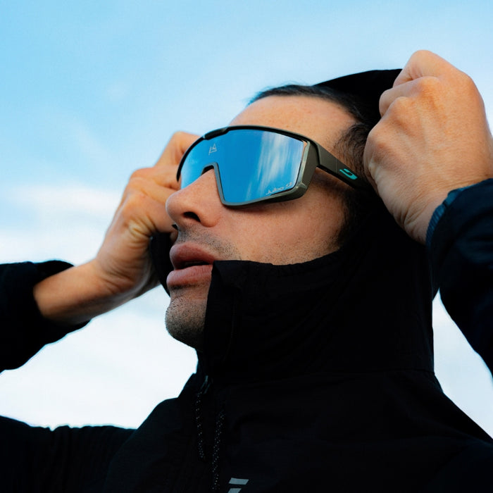 Person adjusting a pair of blue-tinted goggles against a clear sky.