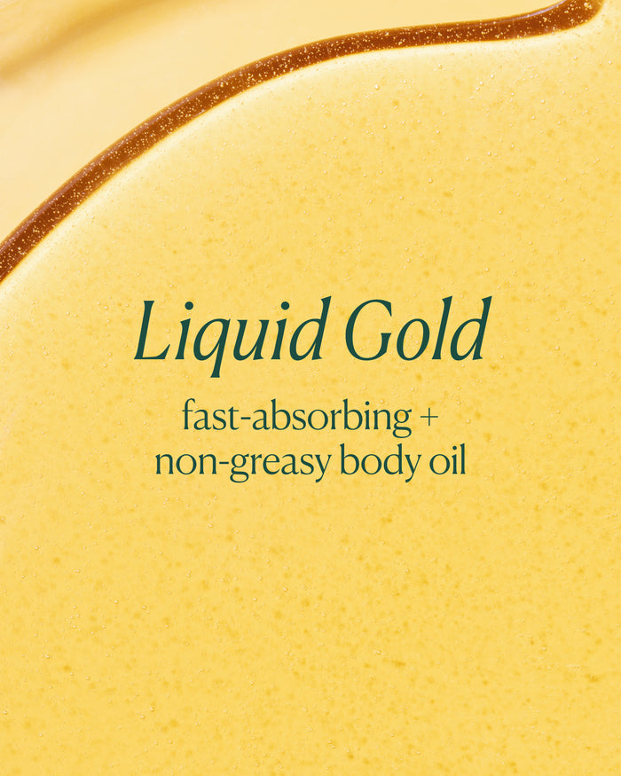 A close-up of a golden yellow liquid body oil with the text 'Liquid Gold' and 'fast-absorbing + non-greasy body oil' printed in dark green on the surface.