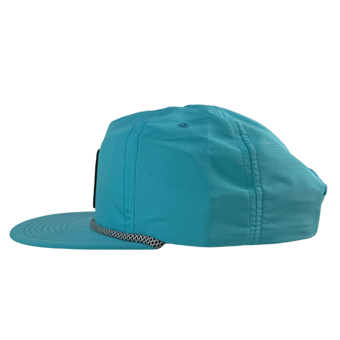 The Julbo Eyewear Né dans les Alpes Unstructured Hat, shown from the side, features turquoise UV-protective fabric, a flat brim, and mesh detail above the brim. #color_né-dans-les-alpes-unstructured-hat-bluebird