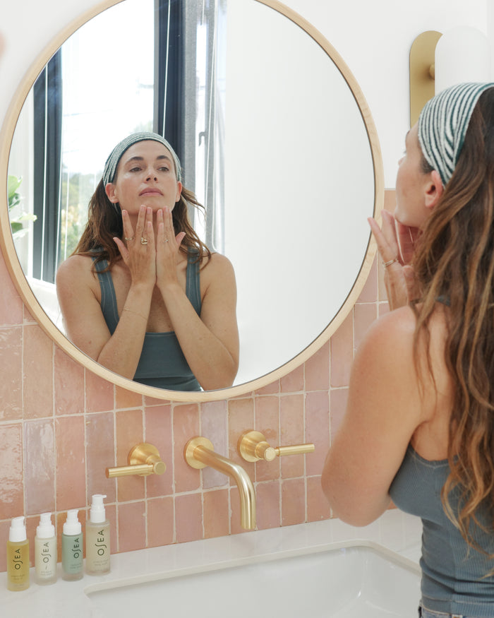 Woman wearing striped headband applying skincare in front of bathroom mirror