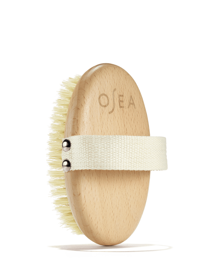 OSEA dry body brush with engraved wooden handle and hand strap on white background
