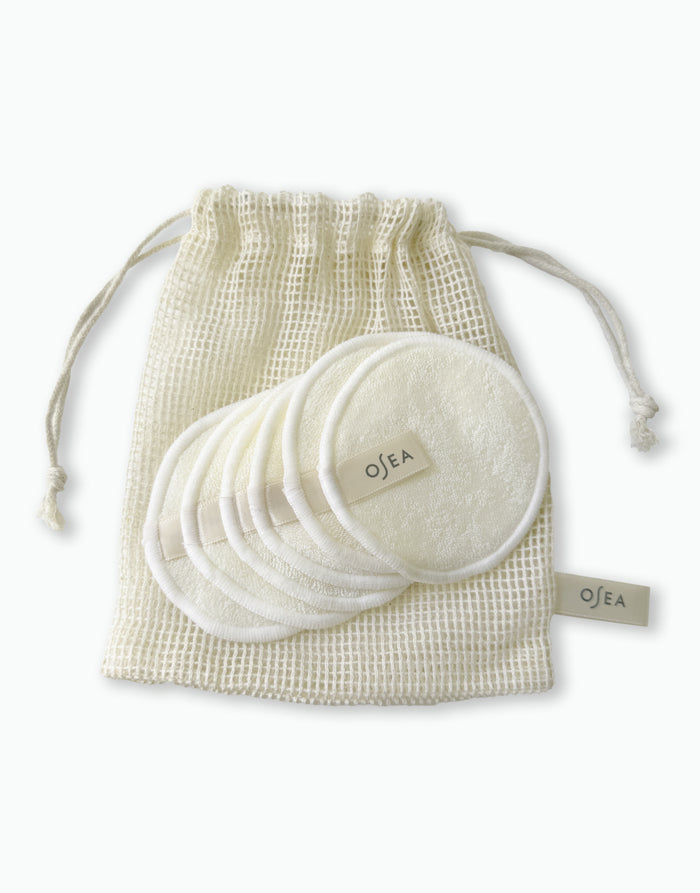 Reusable round OSEA cleansing pads stacked in a cotton mesh drawstring bag on white background