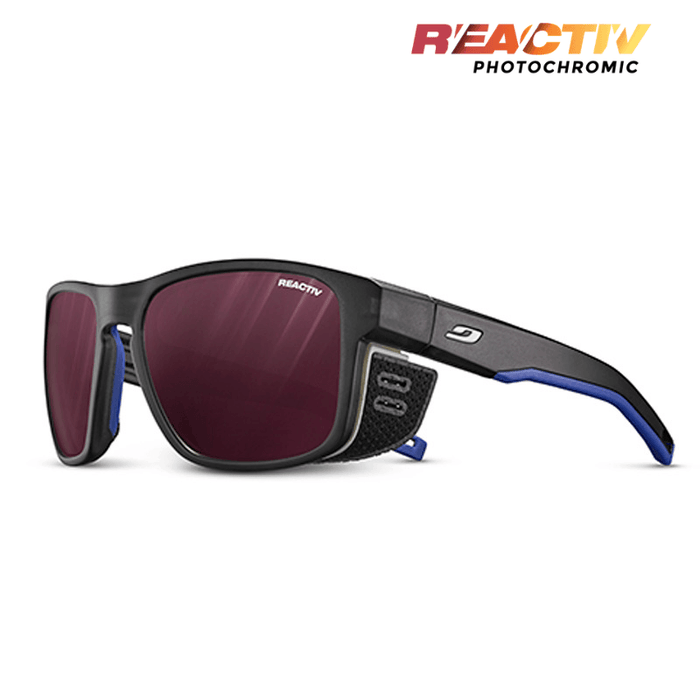 The Julbo-usa Shield sport sunglasses feature black and blue frames, red-tinted REACTIV PHOTOCHROMIC lenses, and side vents—ideal adventure eyewear for your next outdoor journey. #color_translucent-black-blue-white-with-reactiv-0-4-high-contrast-lens