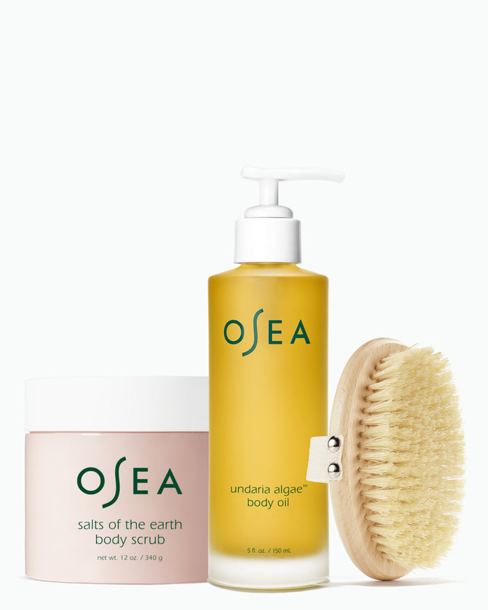 OSEA Undaria Algae™ Body Oil, Salts of the Earth Body Scrub and dry body brush arranged on white background